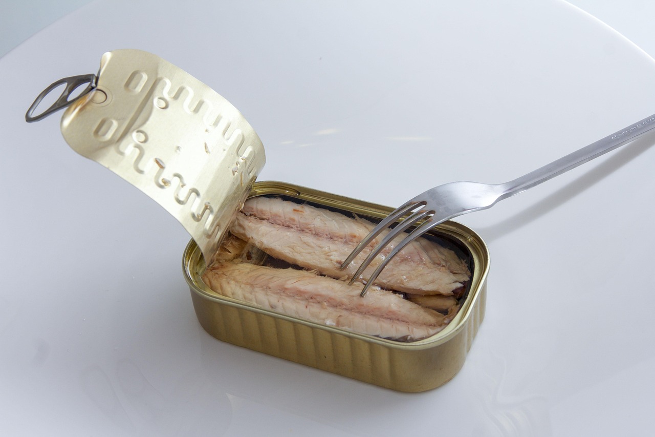 Sgombro in scatola in primo piano su un tavolo, con scatole di diverse marche sullo sfondo.